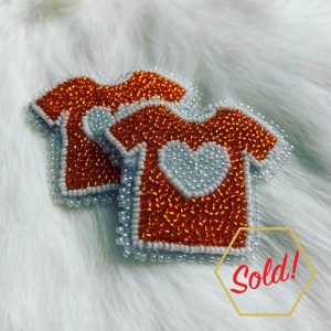 Two beaded orange tshirt pins on a white rabbit fur. Text overlayed says: "sold".