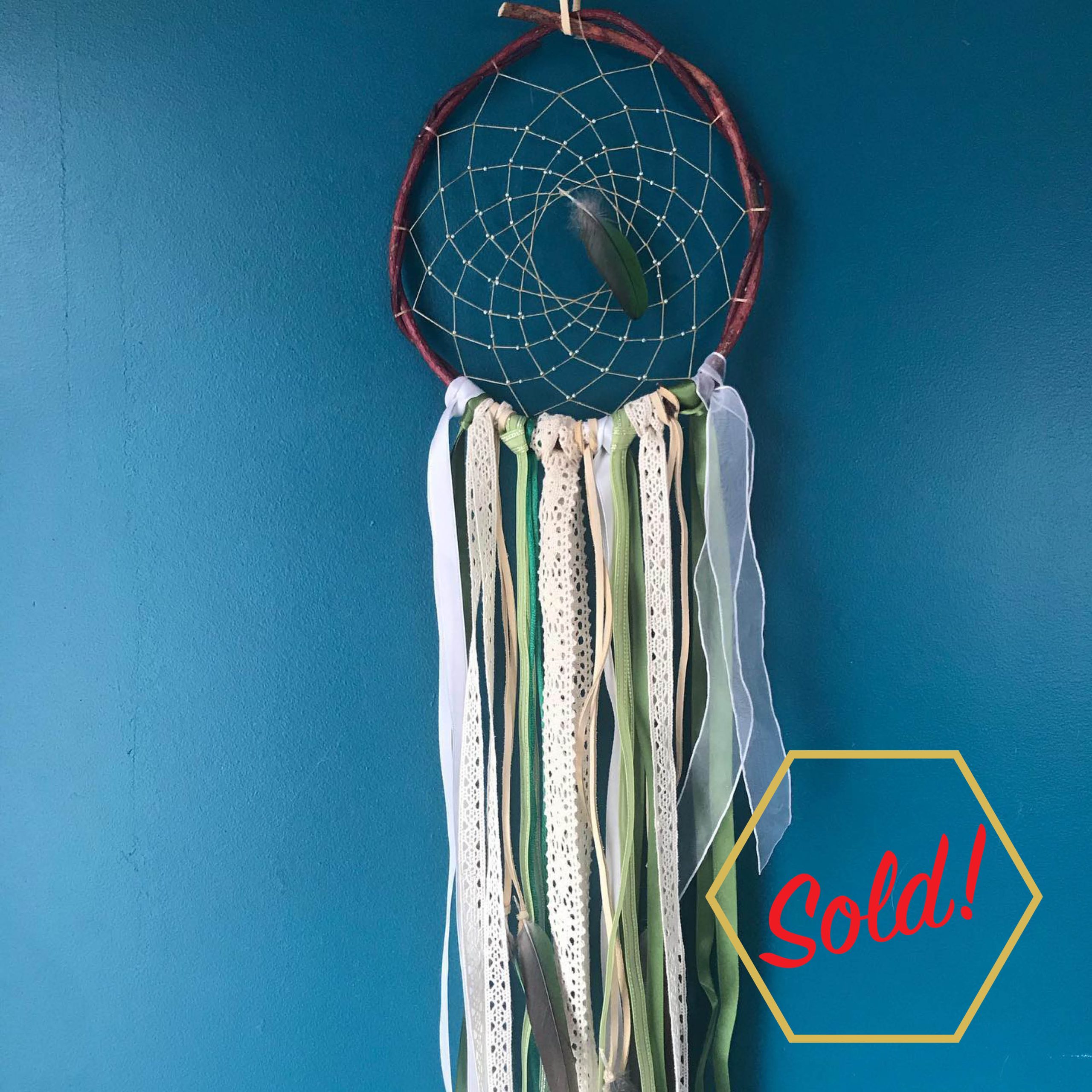 Handmade dreamcatcher with hoop made of red osier dogwood. There are some delicate beads on the webbing. Hanging from the bottom, are some ribbons and lace in white, beige, and green, and green conure feathers. Text overlayed says: "sold".